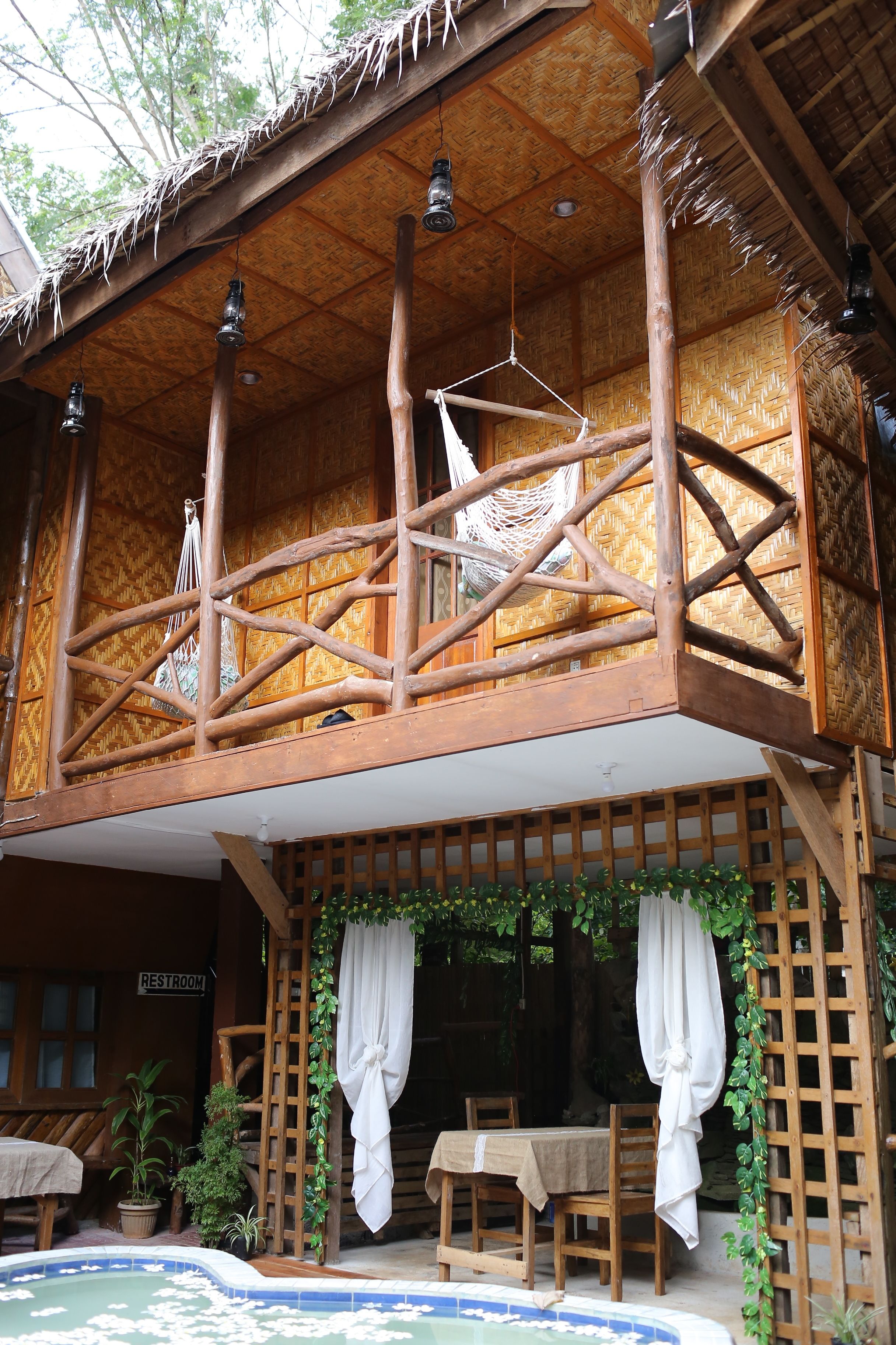 A wooden cabin with a balcony, a pool, and a sign indicating a restroom.