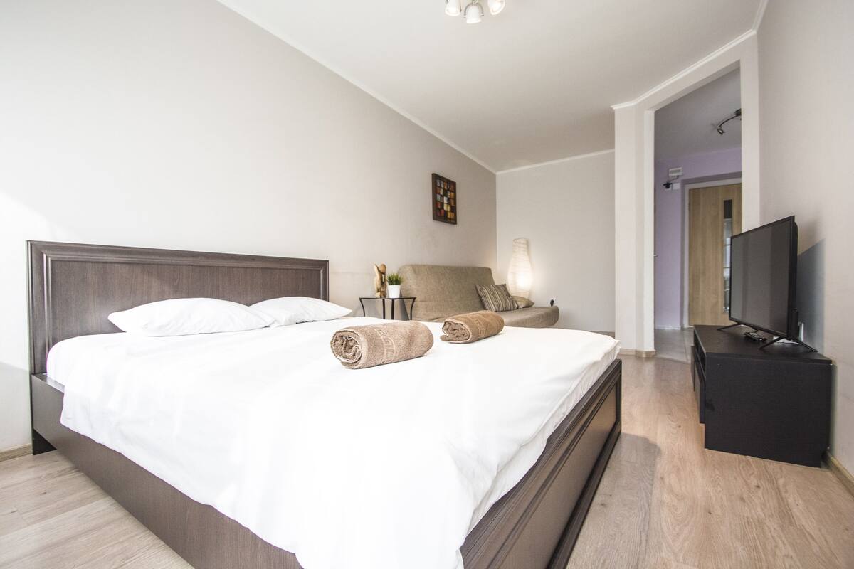 Una habitación de hotel moderna con una cama grande, un televisor de pantalla plana y una mesita de noche con lámpara.