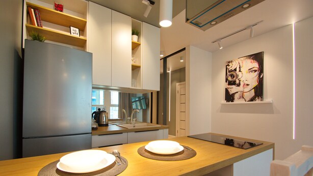 A modern kitchen with a built-in refrigerator, wooden countertops, and a dining area with two white plates and a knife. - Apart Prestige (Minsk)