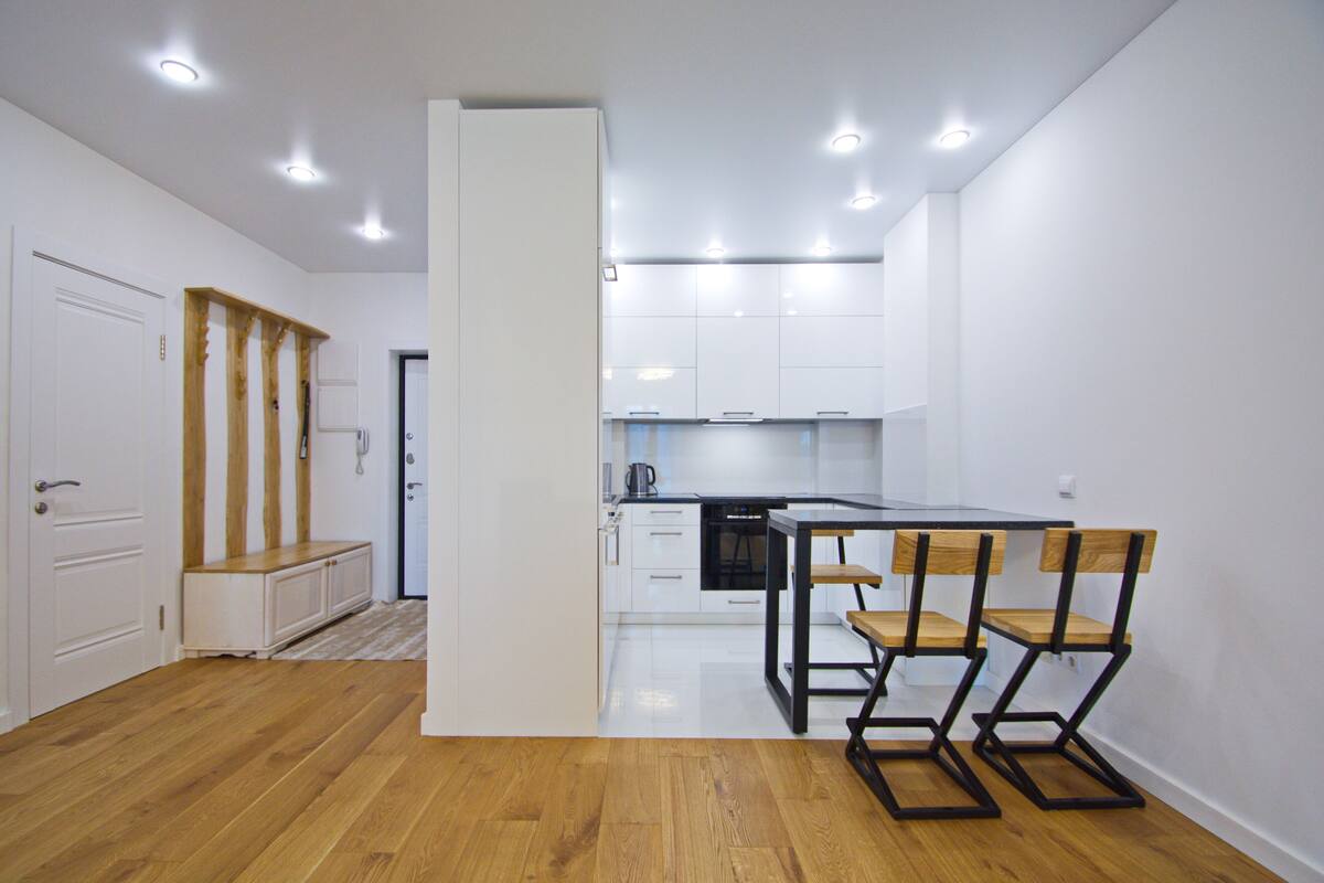 Una cocina moderna con armarios blancos, un banco de madera y una mesa de comedor con sillas.
