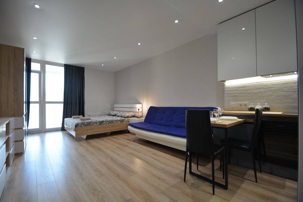 Un dormitorio moderno con cama, sofá azul, escritorio con silla y zona de cocina.