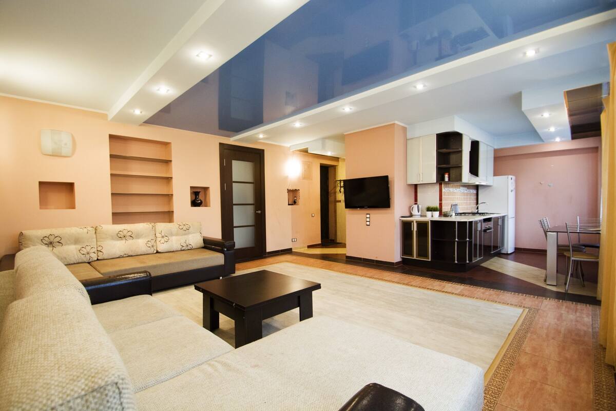 Una sala de estar moderna con un sofá, una mesa de centro y una zona de cocina con armarios y un televisor.