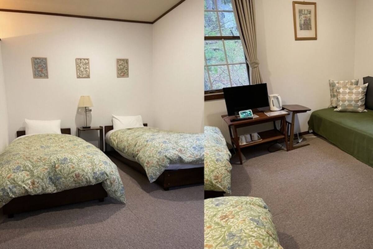 Een hotelkamer met twee enkele bedden, een bureau met een computer, een raam met gordijnen en een klein tafeltje met een waterkoker.