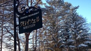 A snow-covered landscape with a sign for a pension/restaurant named Kreutzer.