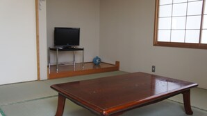 A traditional Japanese room with tatami flooring, a wooden table, a television on a stand, and a window with a grid pattern.