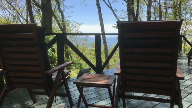 A wooden deck with two chairs and a small table, overlooking a forested area with a clear view of the sky and distant mountains.
