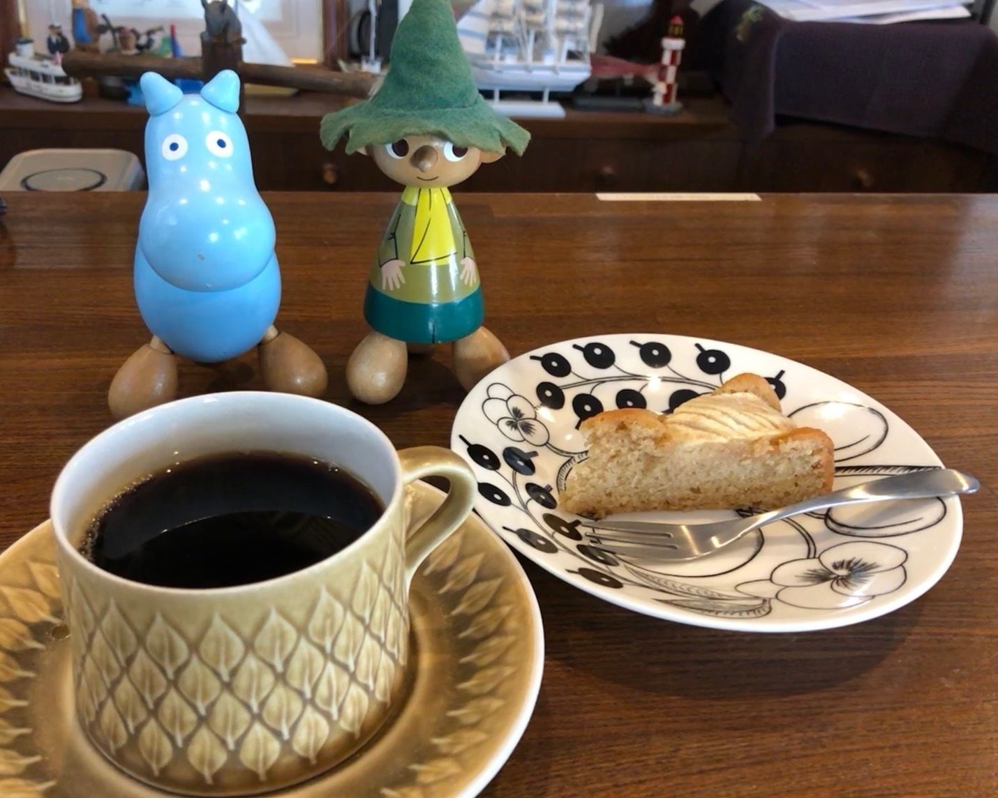 Une tasse de café sur une soucoupe, une part de gâteau sur une assiette et deux statuettes sur une table.