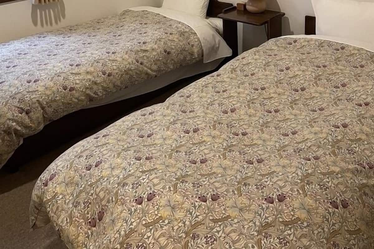 Een kamer met twee bedden, een raam met gordijnen, een nachtkastje met een lamp en een decoratie aan de muur.