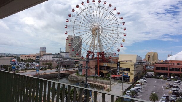 A Ferris wheel in an urban setting with buildings and a parking lot.