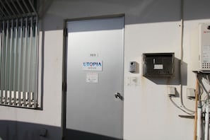 Uma sala de serviços com uma porta identificada como "103 UTOPIA OFFICE" e uma janela com grades de metal.