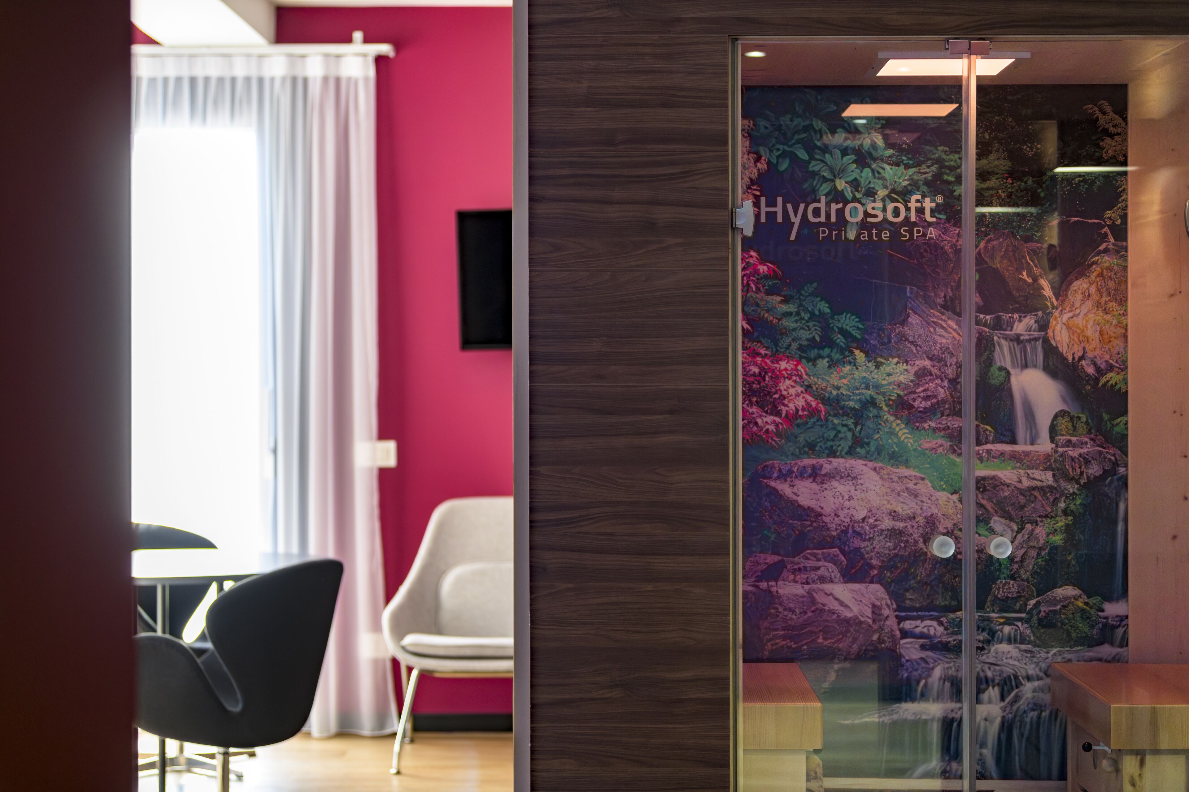 A private spa area with a glass door, a waterfall mural, and a seating area with chairs and a table.
