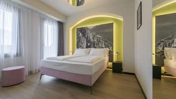 A modern hotel room with a large bed, a pink ottoman, and a mountain view through an arched window.