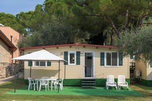 Una casa móvil con facha verde, sillas blancas, una mesa y un paraguas blanco.