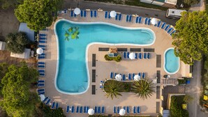 Vue aérienne d’un complexe hôtelier doté d’une grande piscine, de chaises longues et d’un petit espace bar.