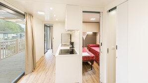 Une pièce compacte dotée d’une kitchenette, d’un lit recouvert d’une courtepointe à motifs rouges et d’une porte-fenêtre coulissante donnant sur un balcon extérieur.