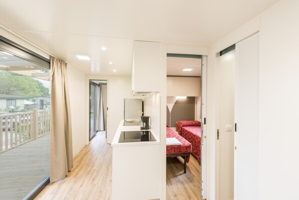 Una habitación compacta con kitchenette, una cama con colcha roja estampada y una puerta corrediza de vidrio que da a un balcón exterior.