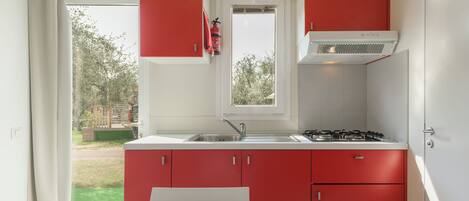 A kitchen with red cabinets, a white countertop, a gas stove, and a window with a view of the outdoors.