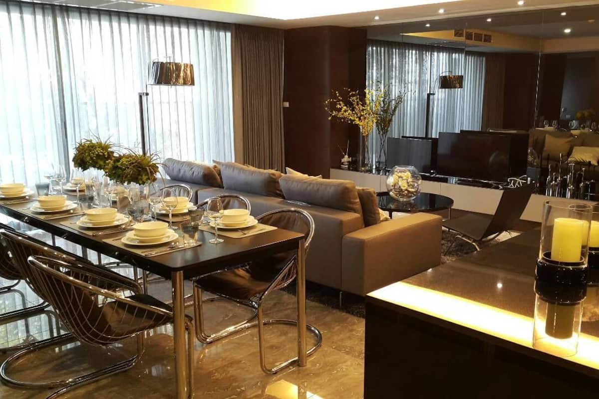 A modern dining area with a long table set for four, a sofa, and a TV in the background.