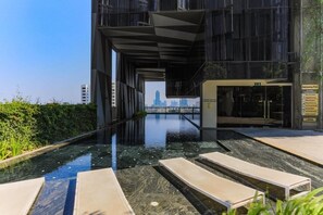 A modern building with a swimming pool, lounge chairs, and a view of the city skyline. - Siamese Ratchakru Residence (Bangkok)
