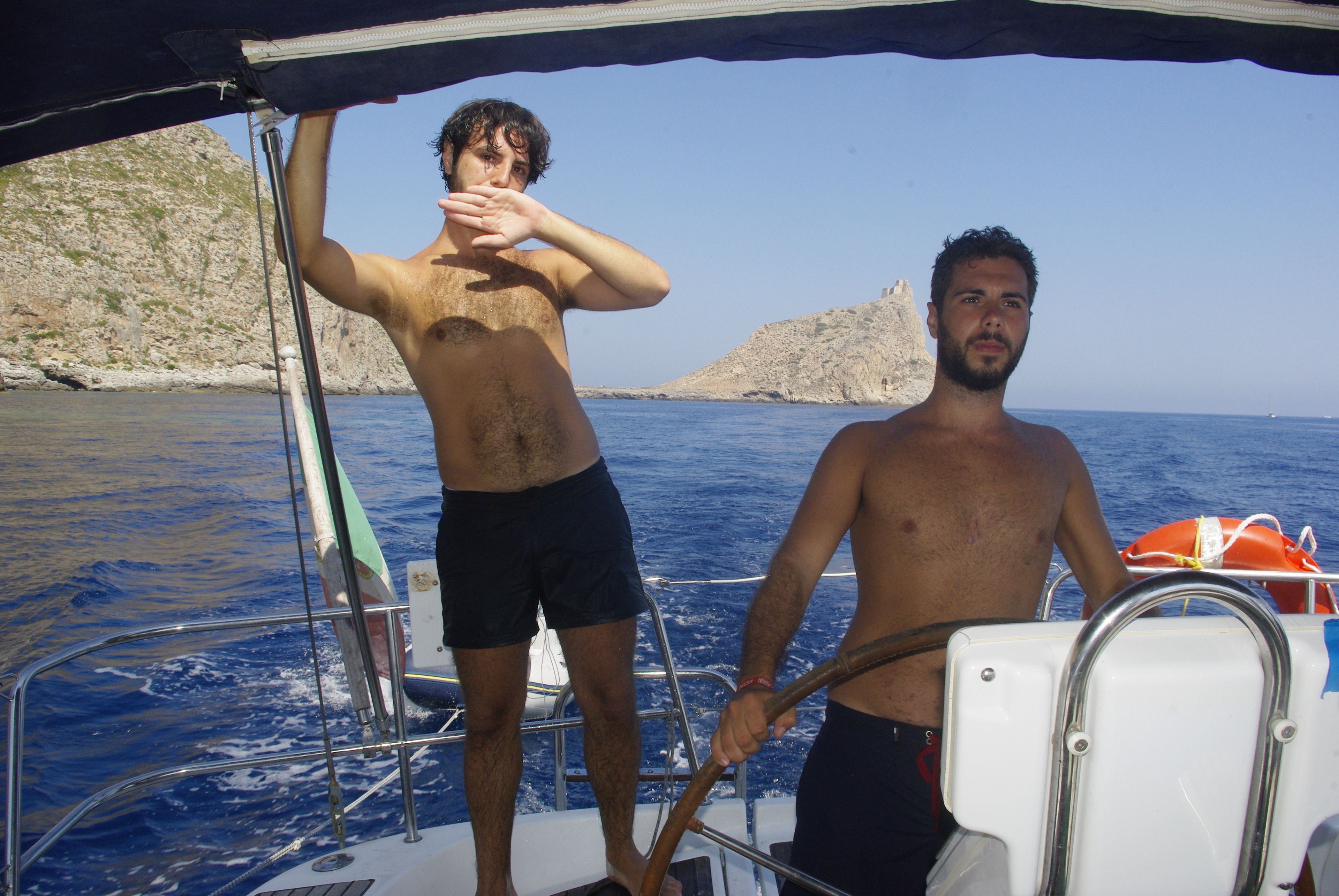Two men on a boat with rocky cliffs in the background.