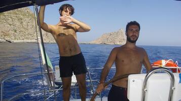 Two men on a boat with rocky cliffs in the background.