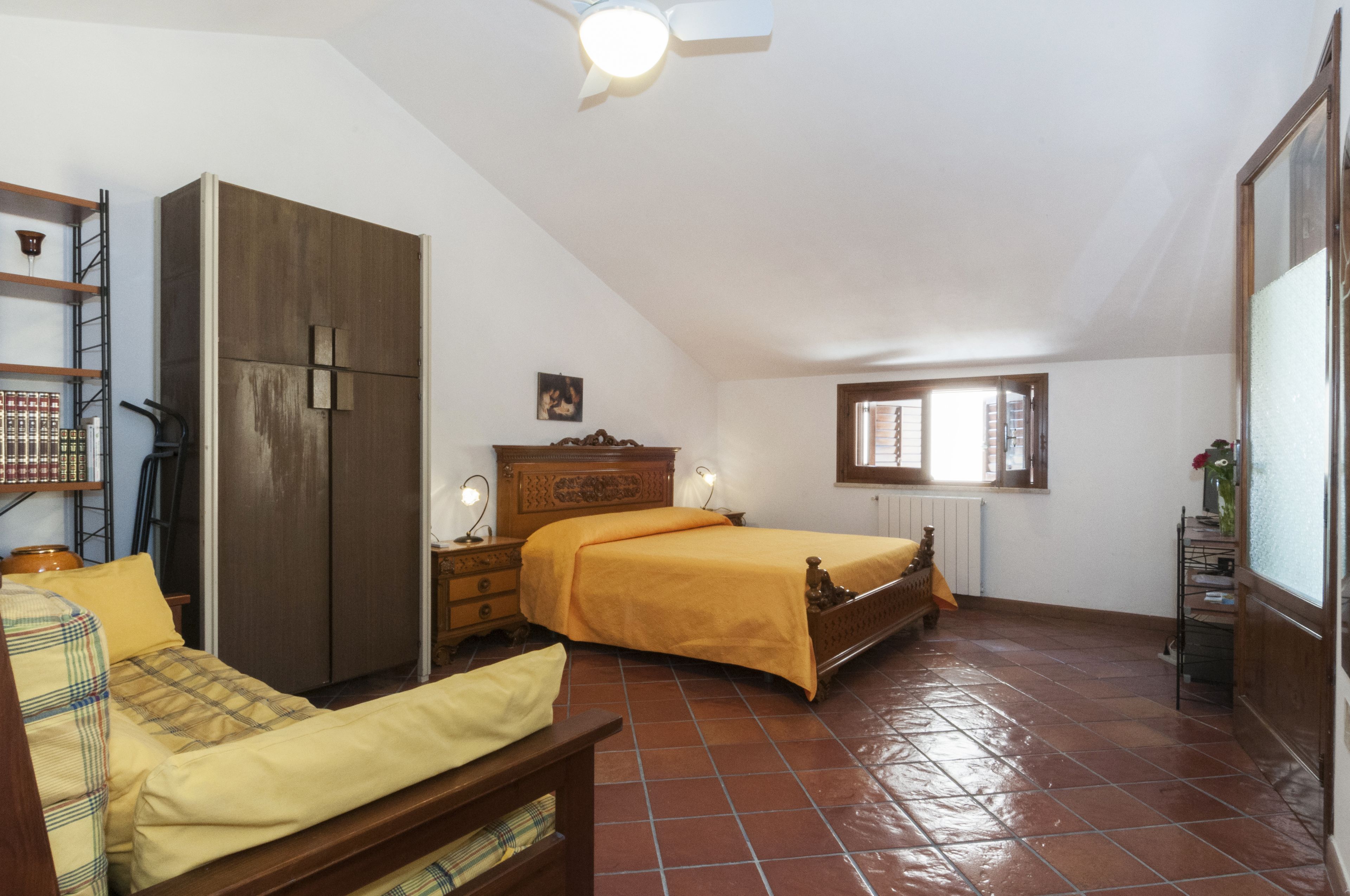 A bedroom with a bed, a wardrobe, a bedside table, and a window.