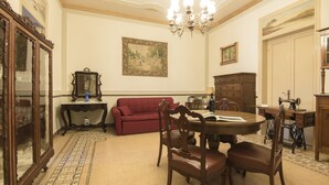 A dining area with a round table, chairs, a red sofa, and a chandelier. - B&B Via Roma (Marsala)
