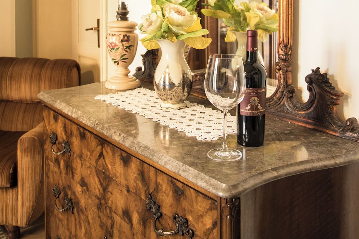 A wooden dresser with a vase of flowers and a wine bottle.