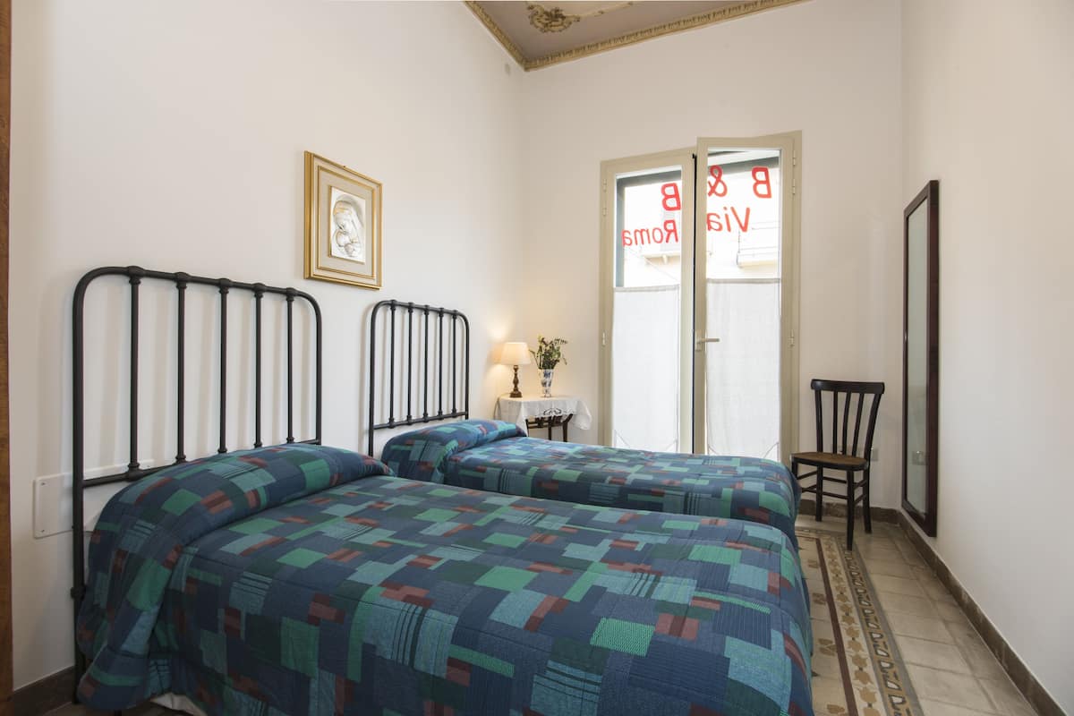 A bedroom with two beds, a framed picture on the wall, a small table with a lamp, and a chair.