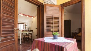 A dining area with a table set for two, a potted plant, and a wooden door leading to another room. - B&B Via Roma (Marsala)