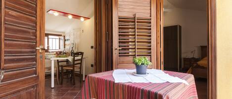 A dining area with a table set for two, a potted plant, and a wooden door leading to another room.