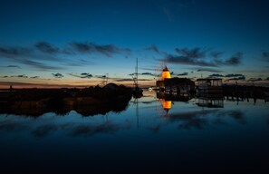 A calm waterfront scene with a windmill and buildings reflecting on the water at dusk.