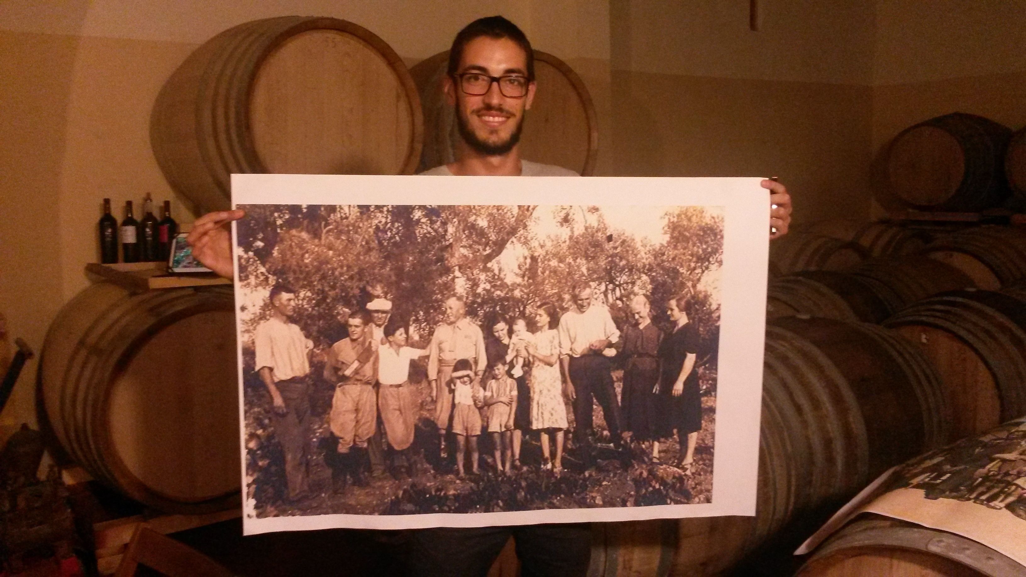A person holding a large photograph in a room with wooden barrels.