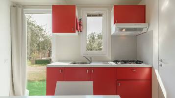 Une cuisine avec des meubles de couleur rouge, un plan de travail blanc, une cuisinière à gaz et une fenêtre donnant sur l’extérieur.