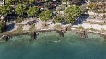 An aerial view of a coastal area with a clear water body, a stone bridge, and a row of trees.