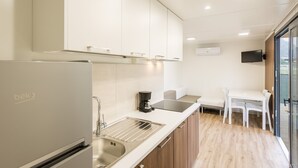 A modern kitchen with a refrigerator, sink, and coffee maker. There is a dining area with a table and chairs.