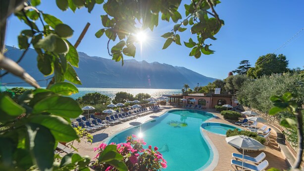A pool area with lounge chairs and umbrellas, surrounded by mountains and a clear sky.