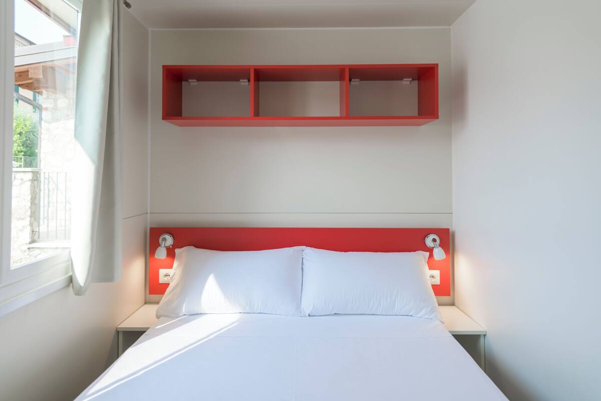 A bedroom with a bed, white pillows, a red headboard, bedside tables, and a window with curtains.