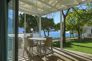 A covered outdoor seating area with a table and chairs, overlooking a body of water and trees. - Camping Park Garda (Limone sul Garda)