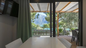 A modern room with a large window, a flat-screen TV mounted on the wall, and a dining area with a table and chairs.