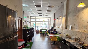 A restaurant with wooden flooring, green and red chairs, and a counter with various items.