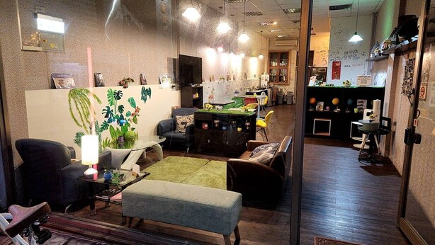 A cozy lounge area with seating, a television, and a green wall with plant decorations.