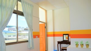 A room with a large window, a door leading outside, a small desk with a mirror, and a wall with a colorful stripe design.