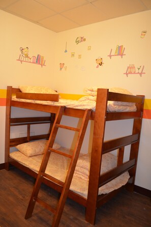 Een stapelbed met een ladder, houten vloer en wanddecoraties, waaronder een boekenplank, een beker en een lachend gezicht.