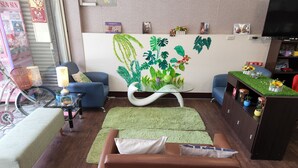A living room with a sofa, a glass coffee table, a lamp, a decorative wall with plant decals, and a television.