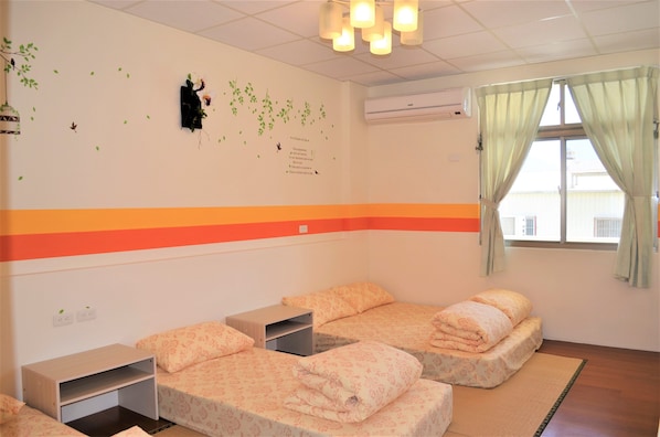 Quarto com duas camas, uma mesa pequena e janela com cortinas.