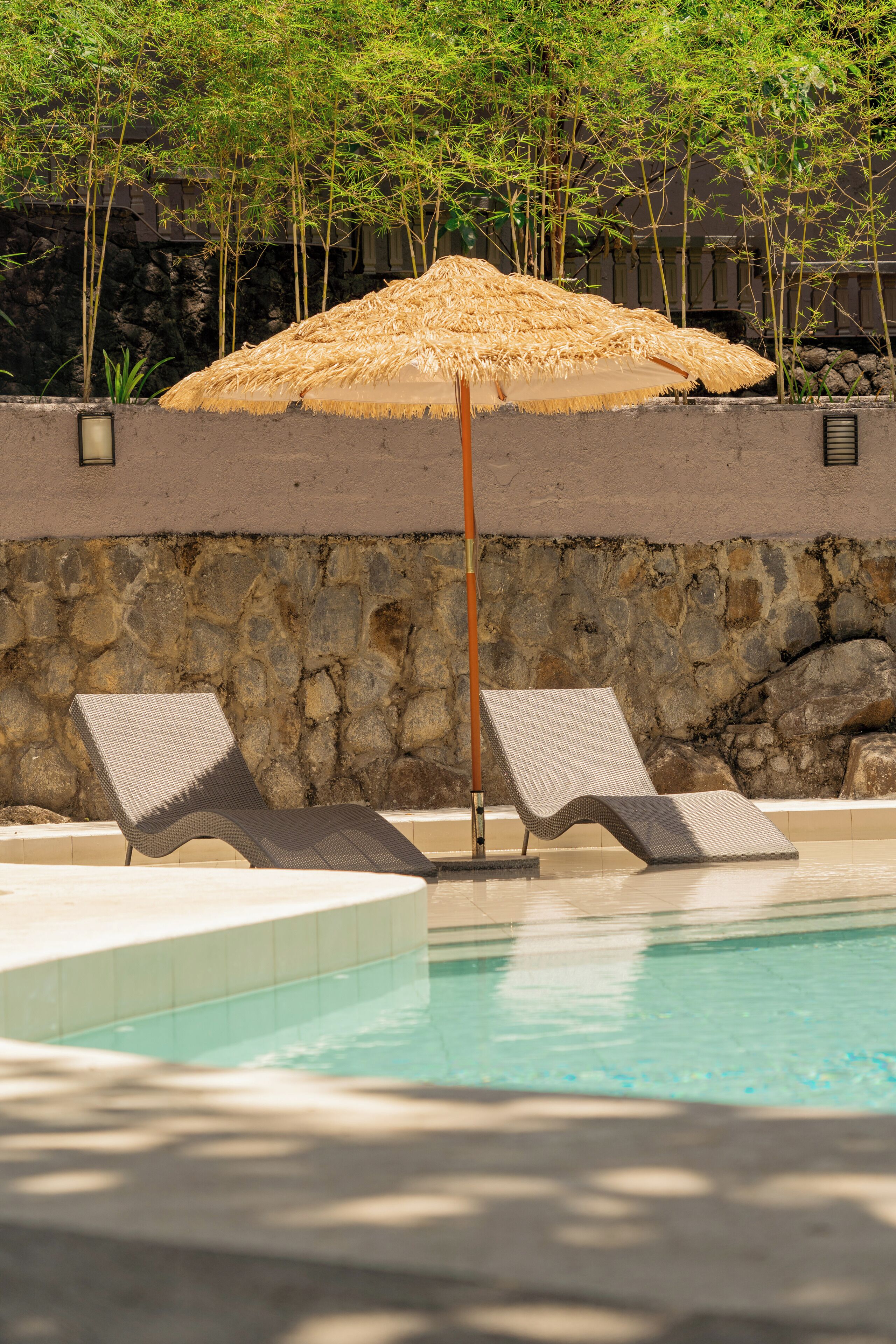 A pool area with two lounge chairs and a straw umbrella.
