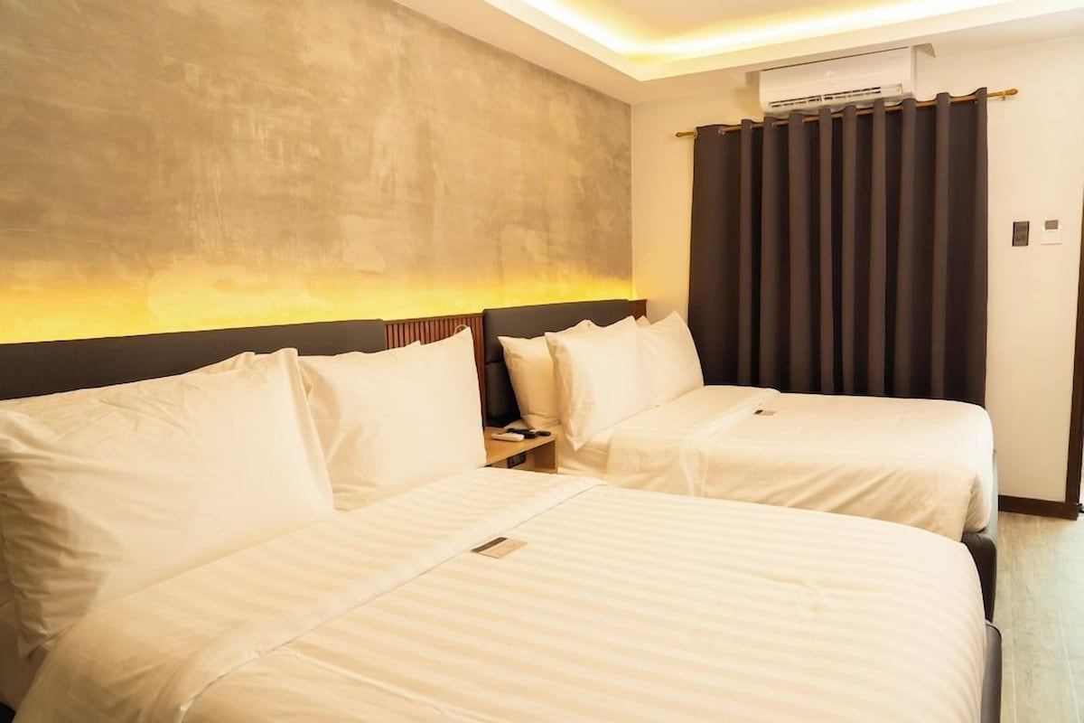 A hotel room with two beds, a headboard, an air conditioning unit, and a curtain.