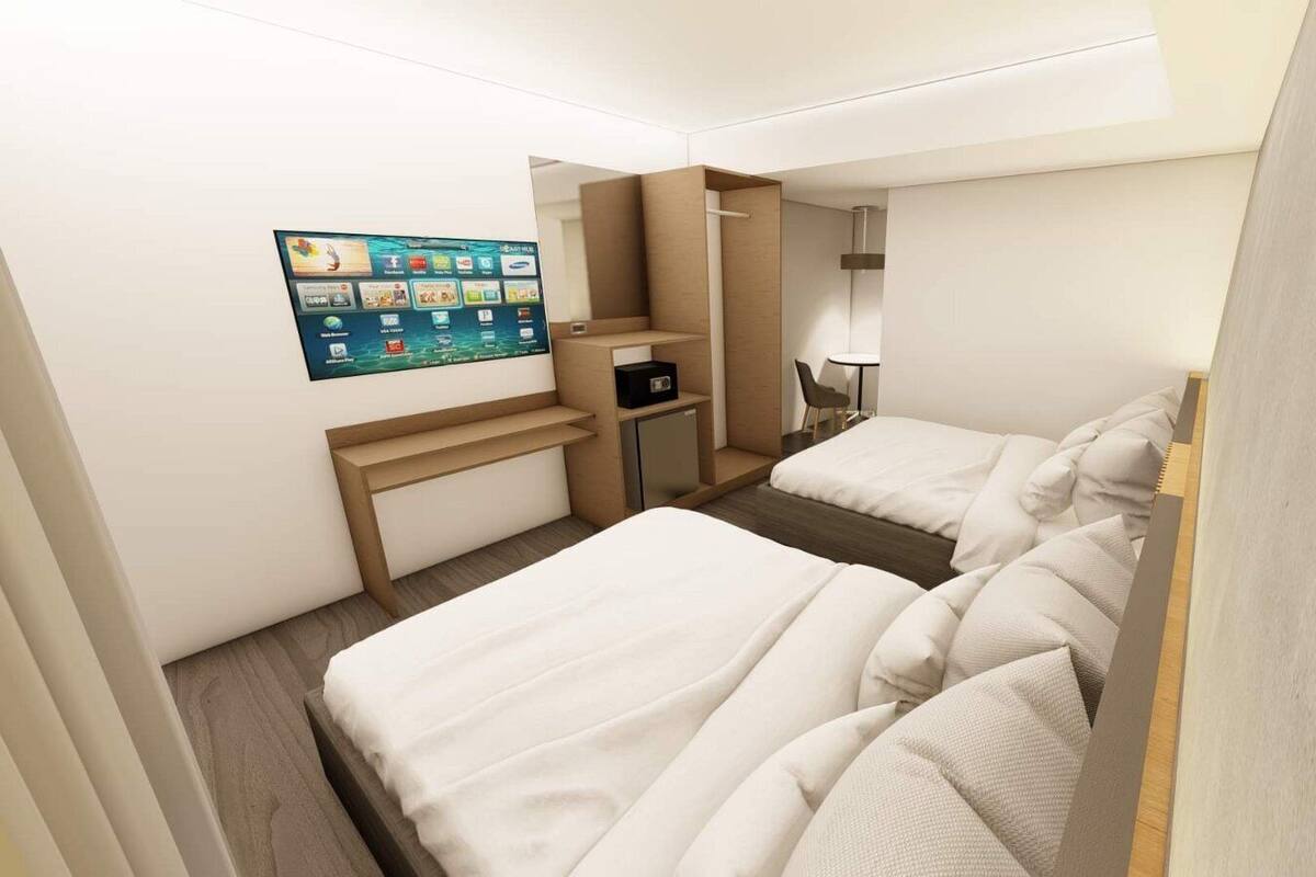 Une chambre d’hôtel avec deux lits, un bureau, une chaise, une petite table et un téléviseur fixé au mur, qui affiche différentes applications.