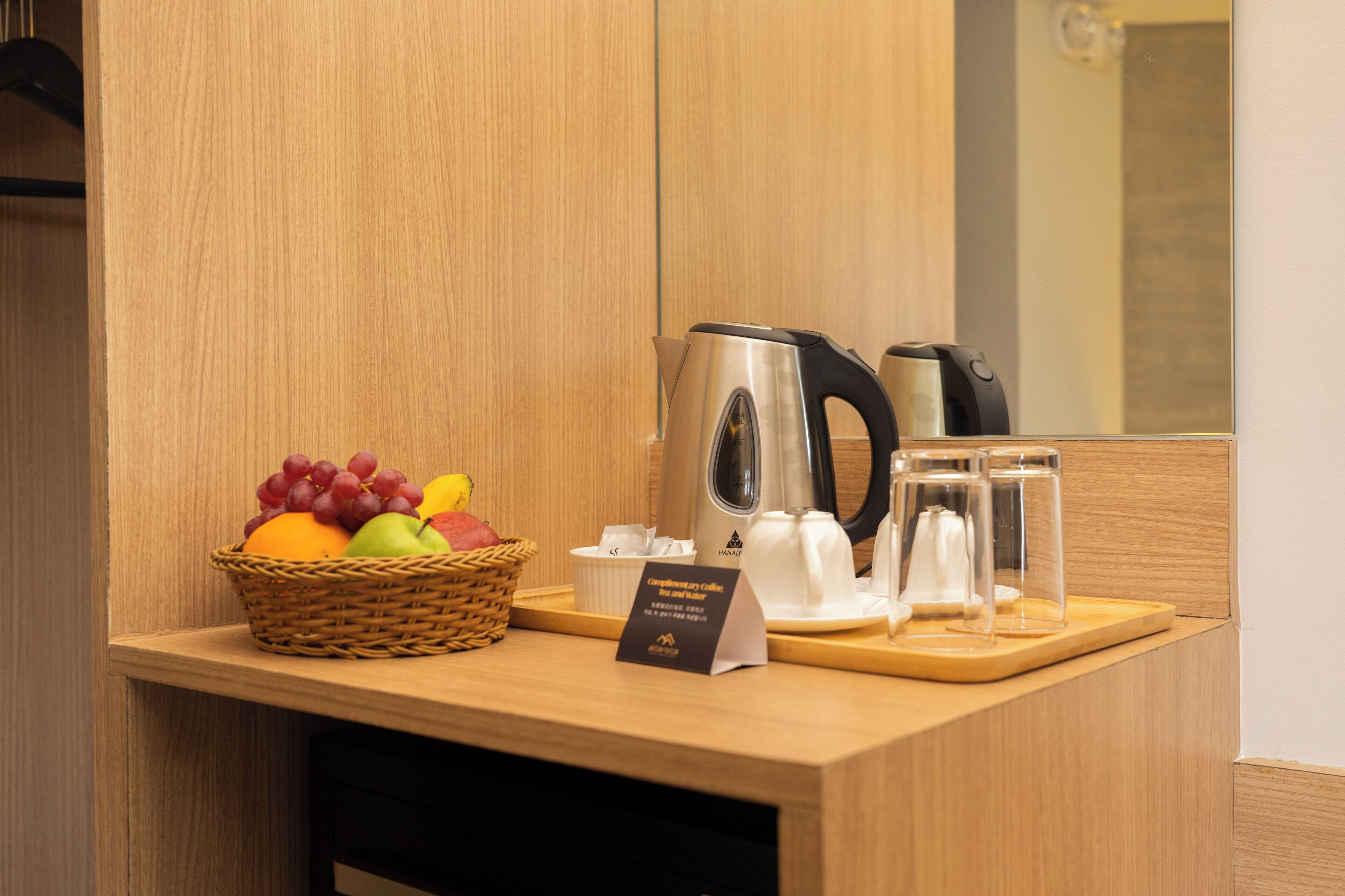 A hotel reception area with a wooden counter, a basket of fruit, a coffee maker, and a tea set.